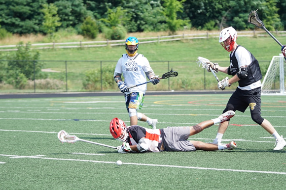 A lacrosse player on the ground while teammates and opponents surround them.