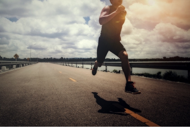 A male athlete running on a road with clouds in the background