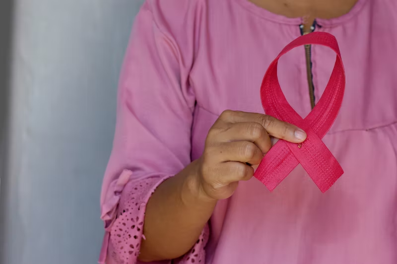 A healthy woman holds up a breast cancer awareness ribbon. 