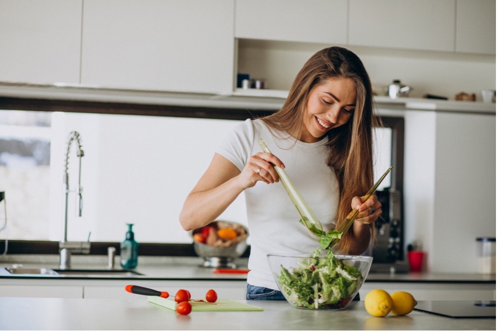 woman tosses a green salad in a white kitchen