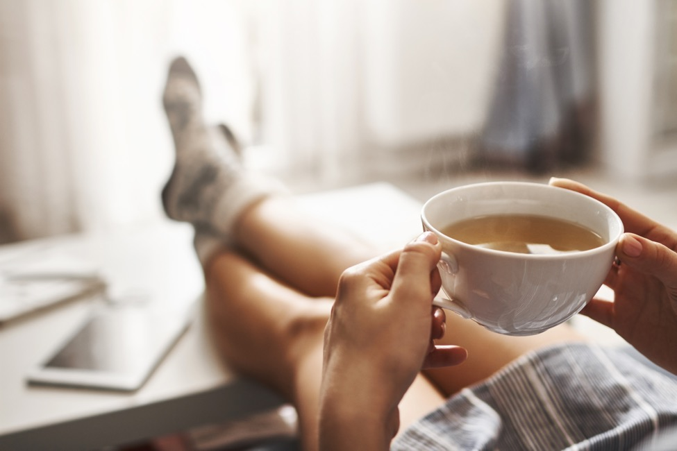 A healthy woman sits with her feet up drinking coffee.