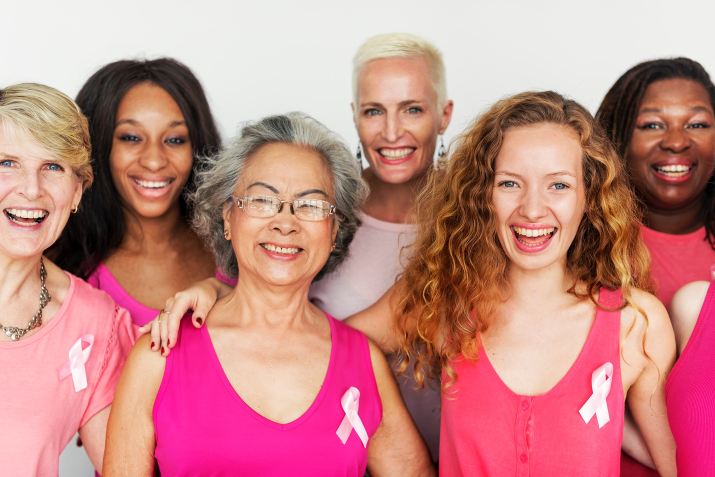 A group of diverse breast cancer survivors wearing pink shirts adorned with light pink ribbons. 
