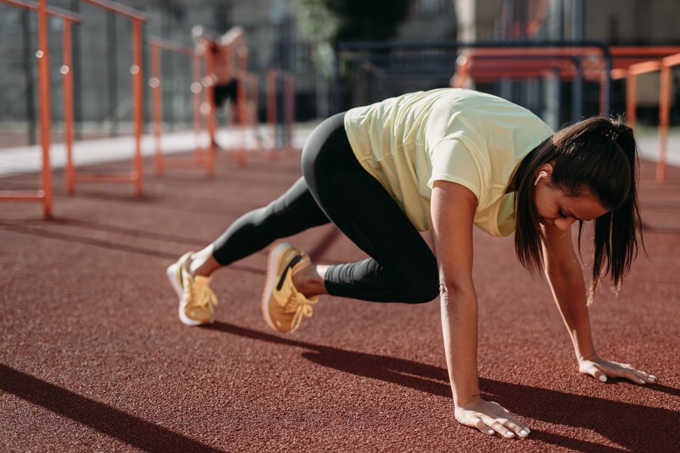 A woman in sportswear stretches on a track to warm up before a run. 