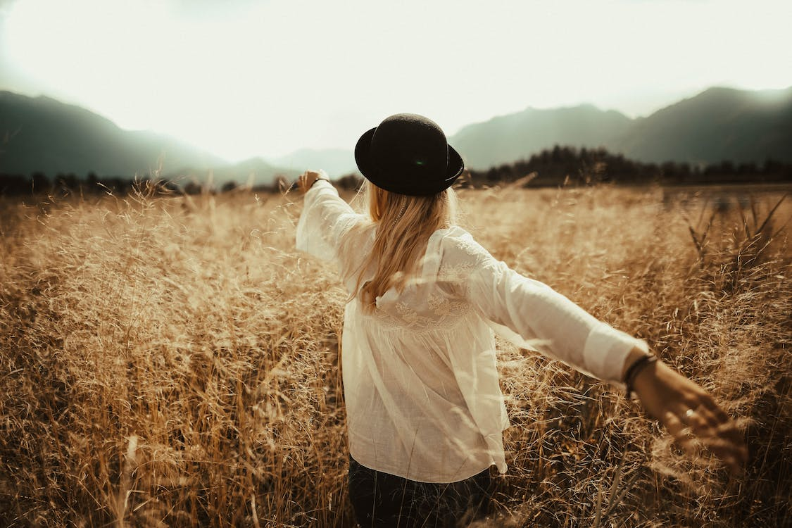 A woman in a bowler hat walking through a field.