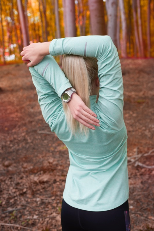 A woman stretches her shoulder in a park. 
