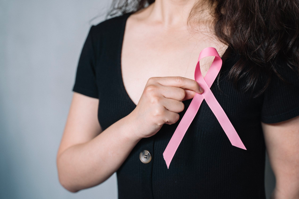 woman wearing a black shirt holds a pink ribbon over her chest
