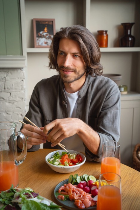  A man with long hair eats a salad with chopsticks.