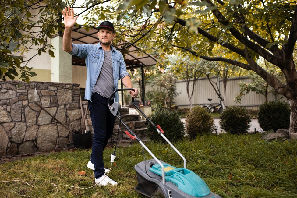 A man waves as he pushes an electric lawn mower